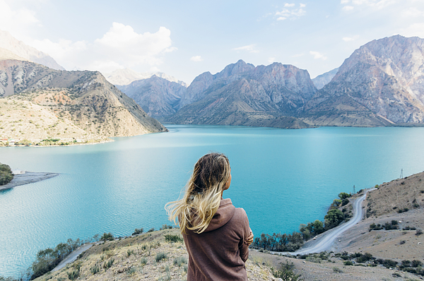 Young woman looks out across mountain lake Photograph by Andrii Lutsyk/ Ascent Xmedia
