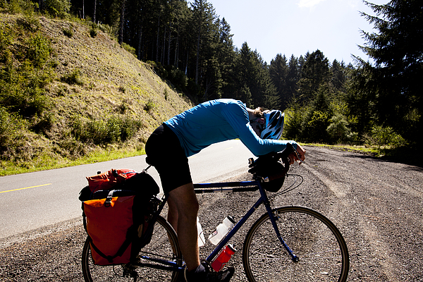 An exhausted male cyclist leans over his touring bike while climbing Mattole Road near Ferndale, California. Photograph by Kyle Sparks