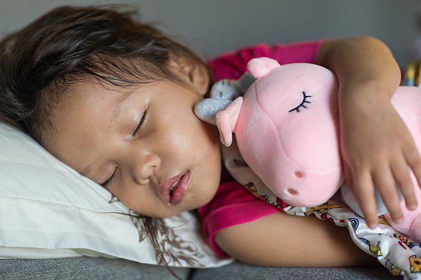 Cute sleeping little asian girl toddler in bed while hugging a stuffed toy. Photograph by PKpix