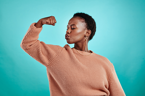 Shot of a beautiful young woman flexing while standing against a turquoise background Photograph by Jeffbergen