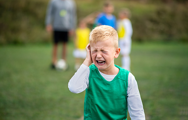 Small boy in pain crying outdoors on football pitch. Photograph by Halfpoint Images