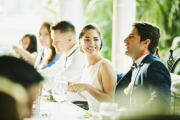 Smiling bride sitting with groom during outdoor wedding reception dinner Photograph by Thomas Barwick