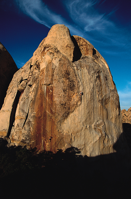 Two Climbers Are Scaling The Side Of A Large Rock Formation With The Sun Shining On The Face Of It And A Blue Sky In The Background Photograph by Rubberball Two Climbers Are Scaling The Side Of A Large Rock Formation With The Sun Shining On The Face Of It And A Blue Sky In The Background Photograph by Rubberball