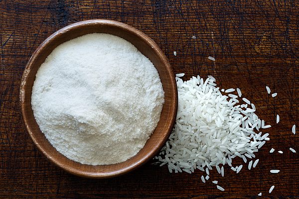 White rice flour in dark wooden bowl isolated on dark brown wood from above. Spilled rice. Photograph by Etienne Voss