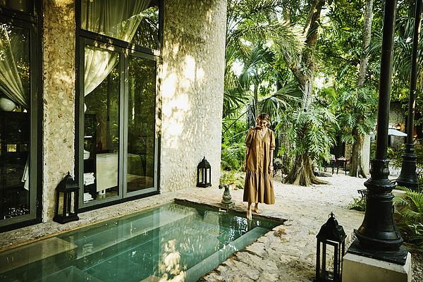 Wide shot of smiling woman standing pool and putting foot in water at luxury tropical spa Photograph by Thomas Barwick