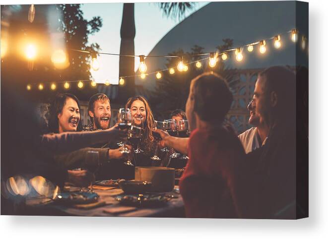 Asian And Indian Ethnicities Canvas Print featuring the photograph Happy family dining and tasting red wine glasses in barbecue dinner party - People with different ages and ethnicity having fun together - Youth and elderly parents and food weekend activities concept by Alessandro Biascioli