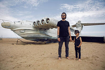 Musicians Photo Rights Managed Images - Family A Boy And His Father In Rocker Clothes Stand At An Abandoned Ekranoplan Plane Royalty-Free Image by Elena Saulich
