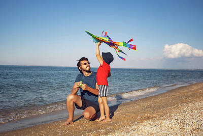 Vintage Food Signs Royalty Free Images - Father And Son Are Standing On A Sandy Beach By The Sea And Launch Toy Striped Kite In The Summer On Vacation Royalty-Free Image by Elena Saulich