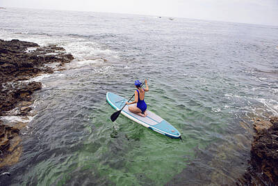 Athletes Photos - athlete woman in a blue swimsuit and bandana on stand up paddle board on a quiet blue ocean. Sup surfing in water by Elena Saulich