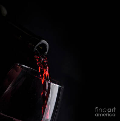 Wine Royalty-Free and Rights-Managed Images - Red wine pouring in wineglass from bottle over black background. by Jelena Jovanovic